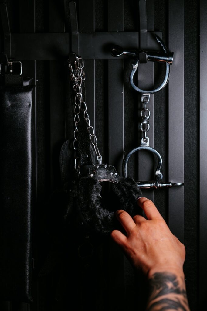 Na ciemnej ścianie wiszą różne akcesoria BDSM, w tym metalowe kajdanki